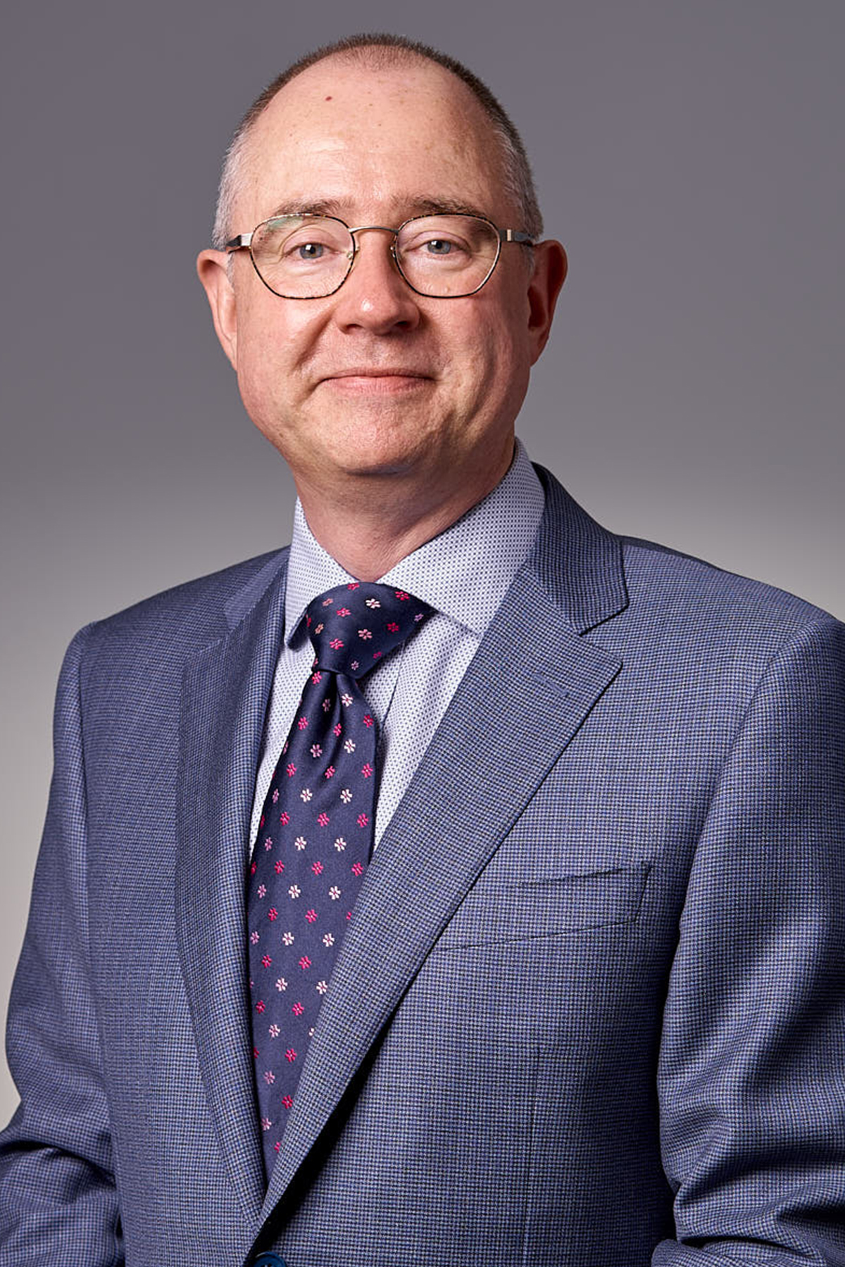 Mark de Raad is a man in his fifties with short dark hair, round glasses and is wearing a grey suit.